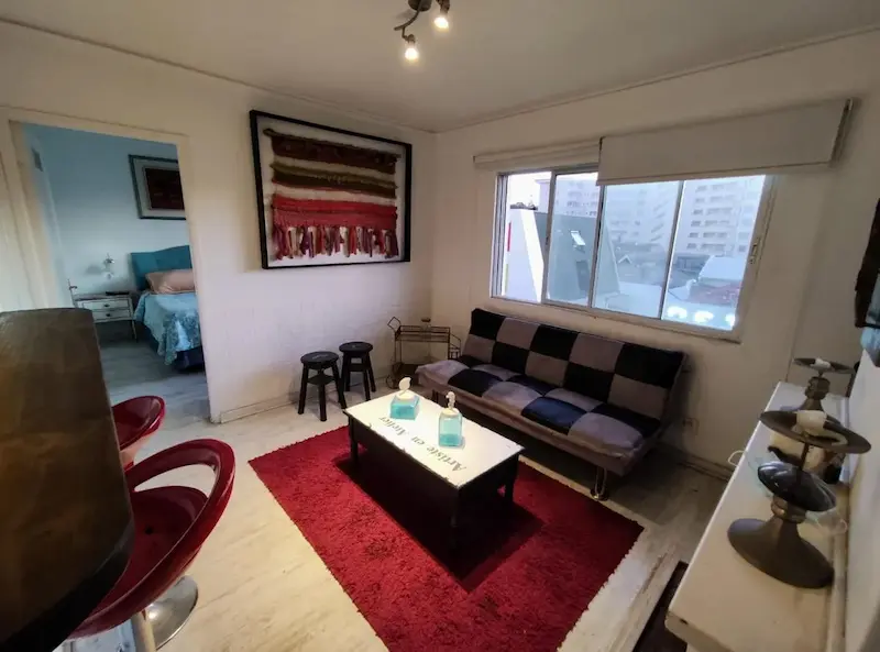 Vista interior del departamento con alfombra roja, asientos, cama matrimonial y un sofá