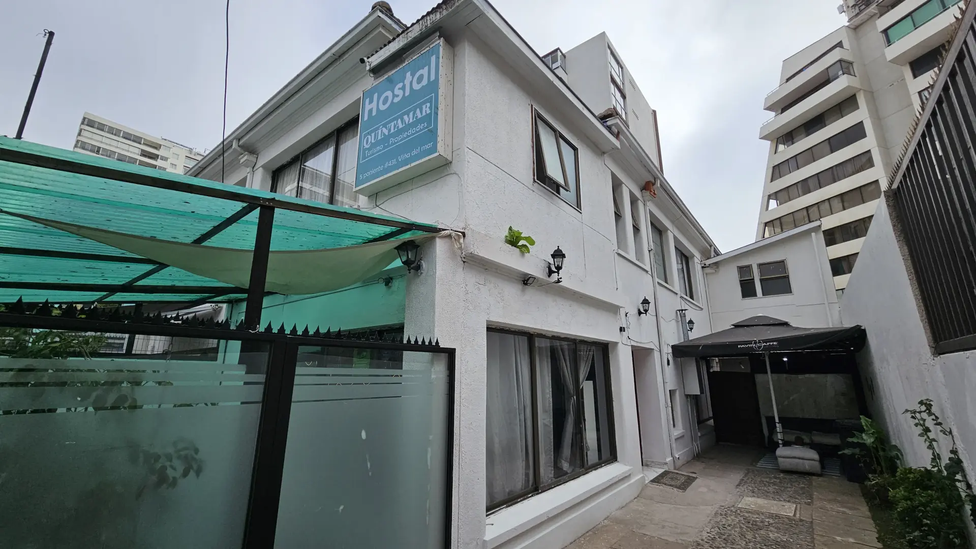 Vista exterior del Hostal Turismo Quintamar, con un cartel que muestra el nombre del hostal y una zona exterior con asientos para los pasajeros