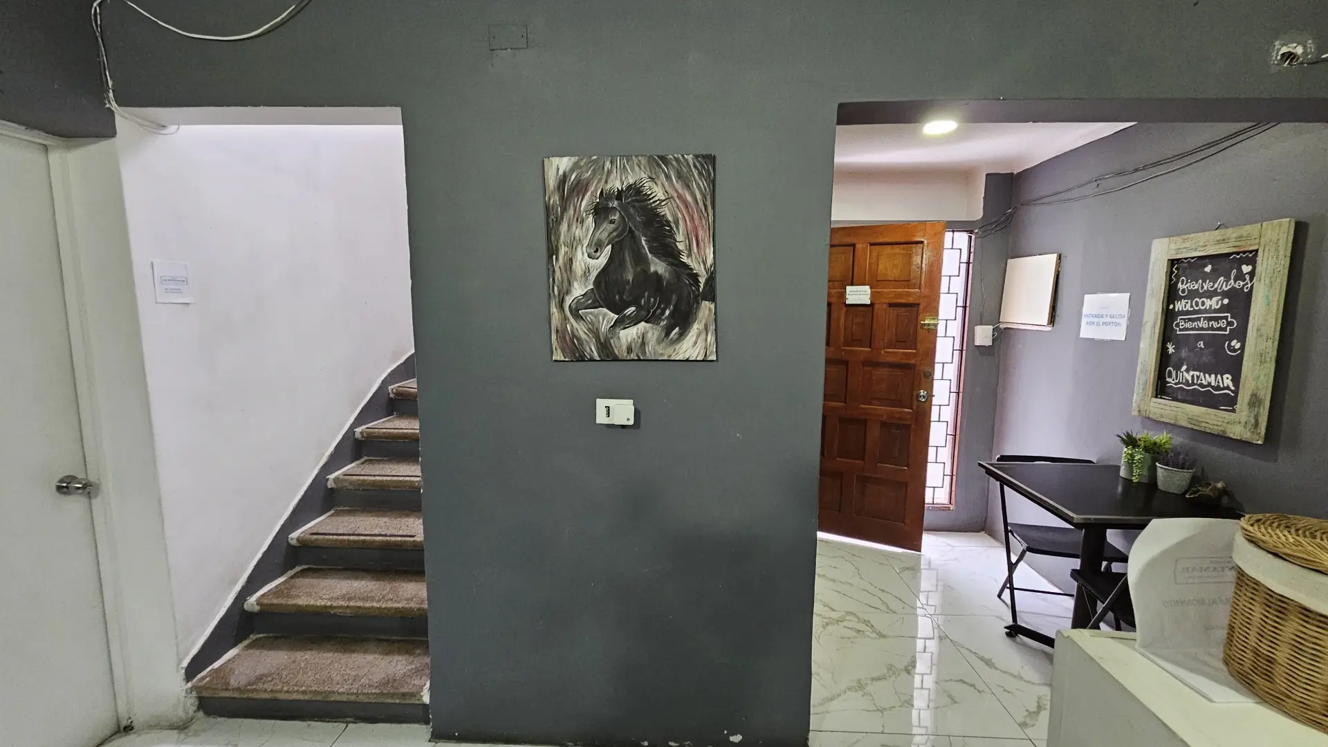 Escalera ubicada en la recepción, con un cuadro de un caballo y otro de bienvenida