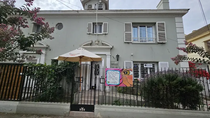 Fachada del Hostal Casona del Mar, un edificio de 3 pisos con reja negra y un cartel que anuncia servicios de uñas como esmaltado y manicura